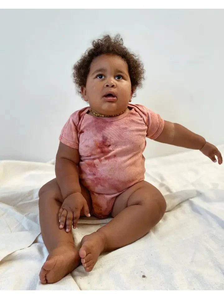 Baby wearing Organic Canyon Onesie in pink, hand-dyed with organic cotton for comfort and sustainability.