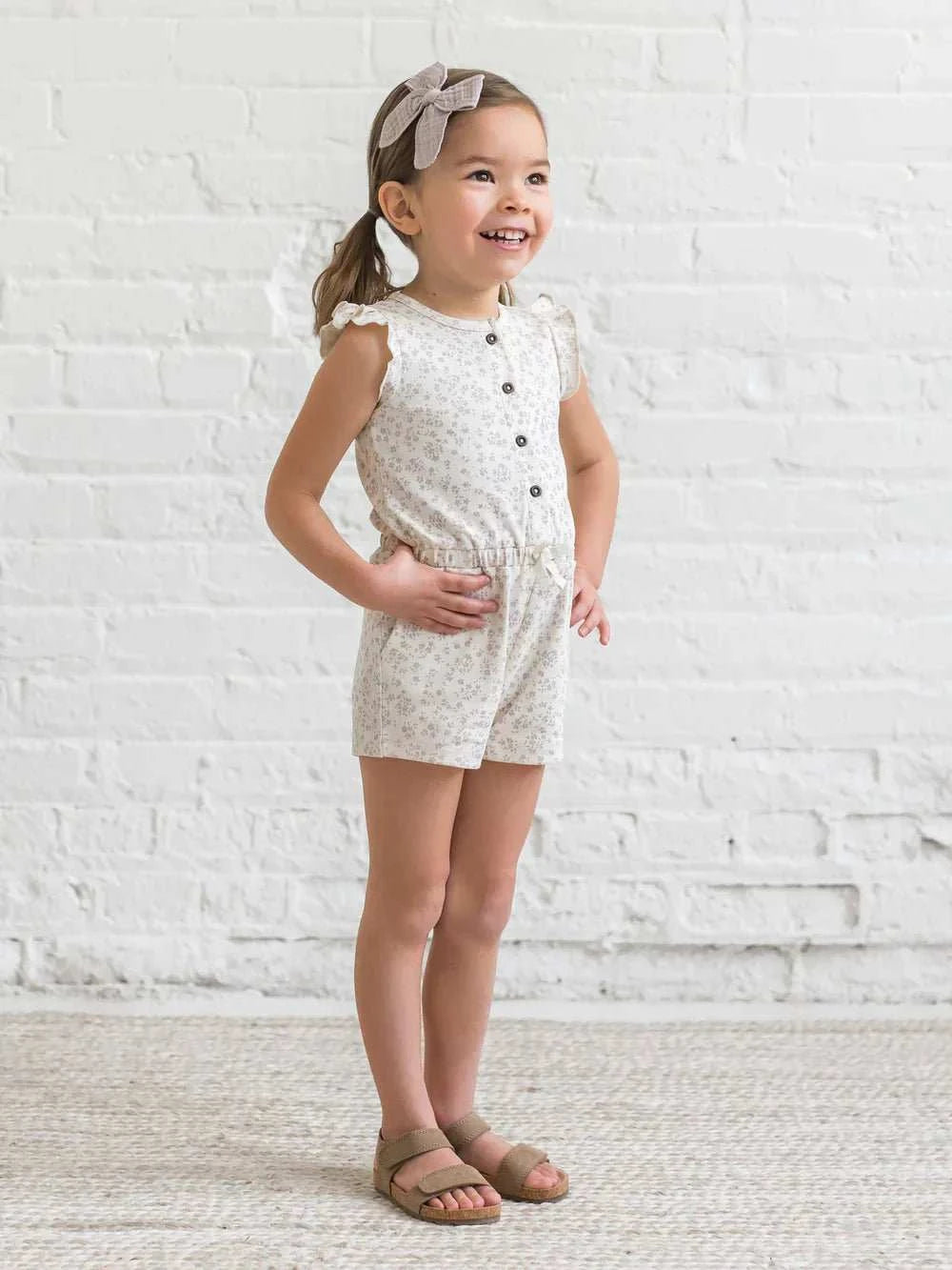 Girl wearing Shaye Romper with coconut buttons and flutter sleeves, made of organic cotton.