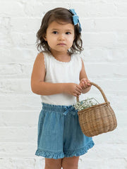 Child wearing Callie Chambray Ruffle Waist Short with basket, white background.